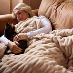 Woman lying on a couch with a cat, wrapped in a beige blanket in a cozy room.