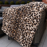 Leopard print blanket draped over a wicker chair on a patio with outdoor lighting and plants in the background.