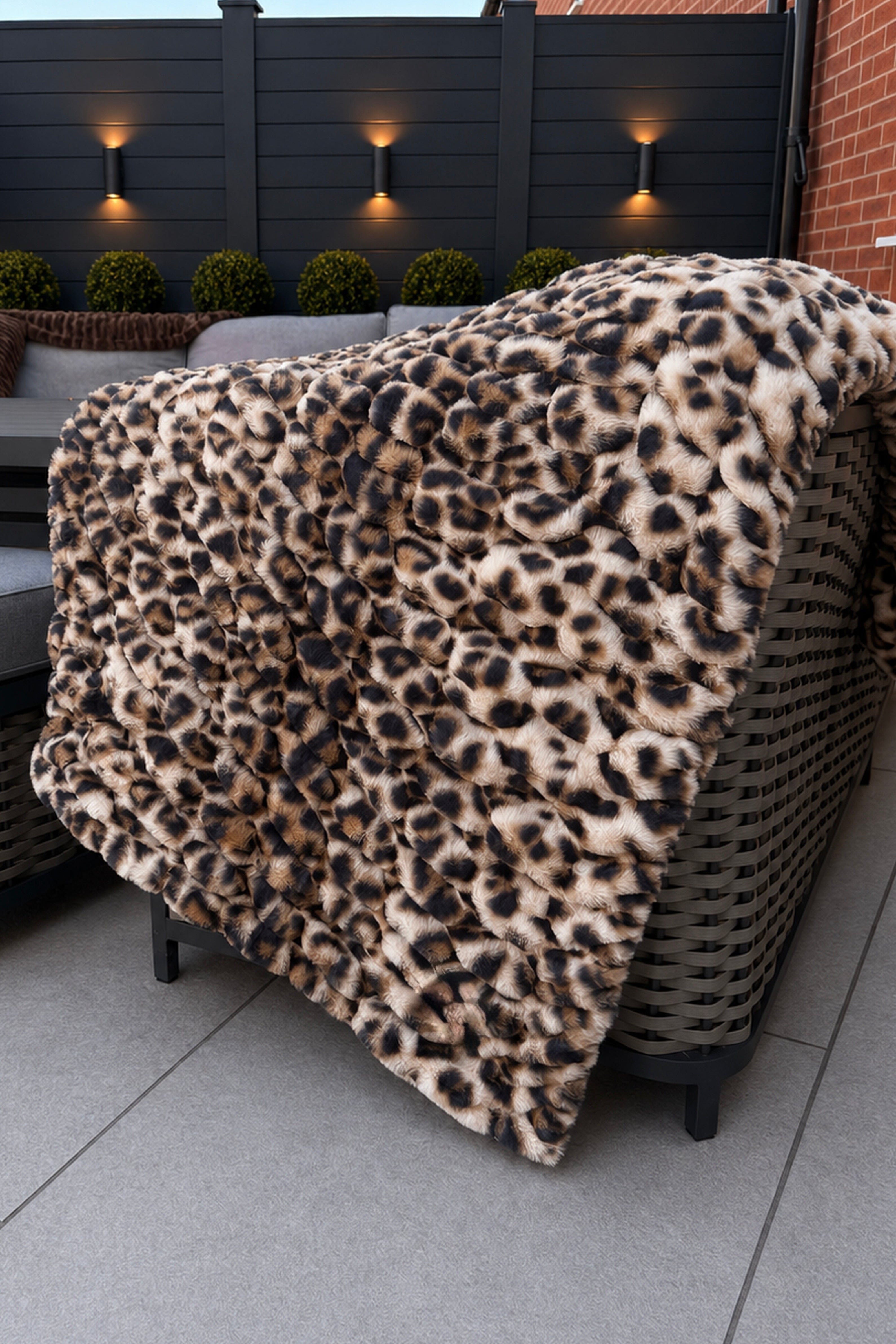 Leopard print blanket draped over a wicker chair on a patio with outdoor lighting and plants in the background.
