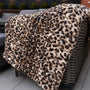 Leopard print blanket draped over a wicker chair on a patio with outdoor lighting and plants in the background.