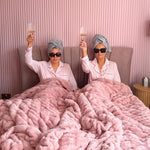 Two women in bed with pink blankets.