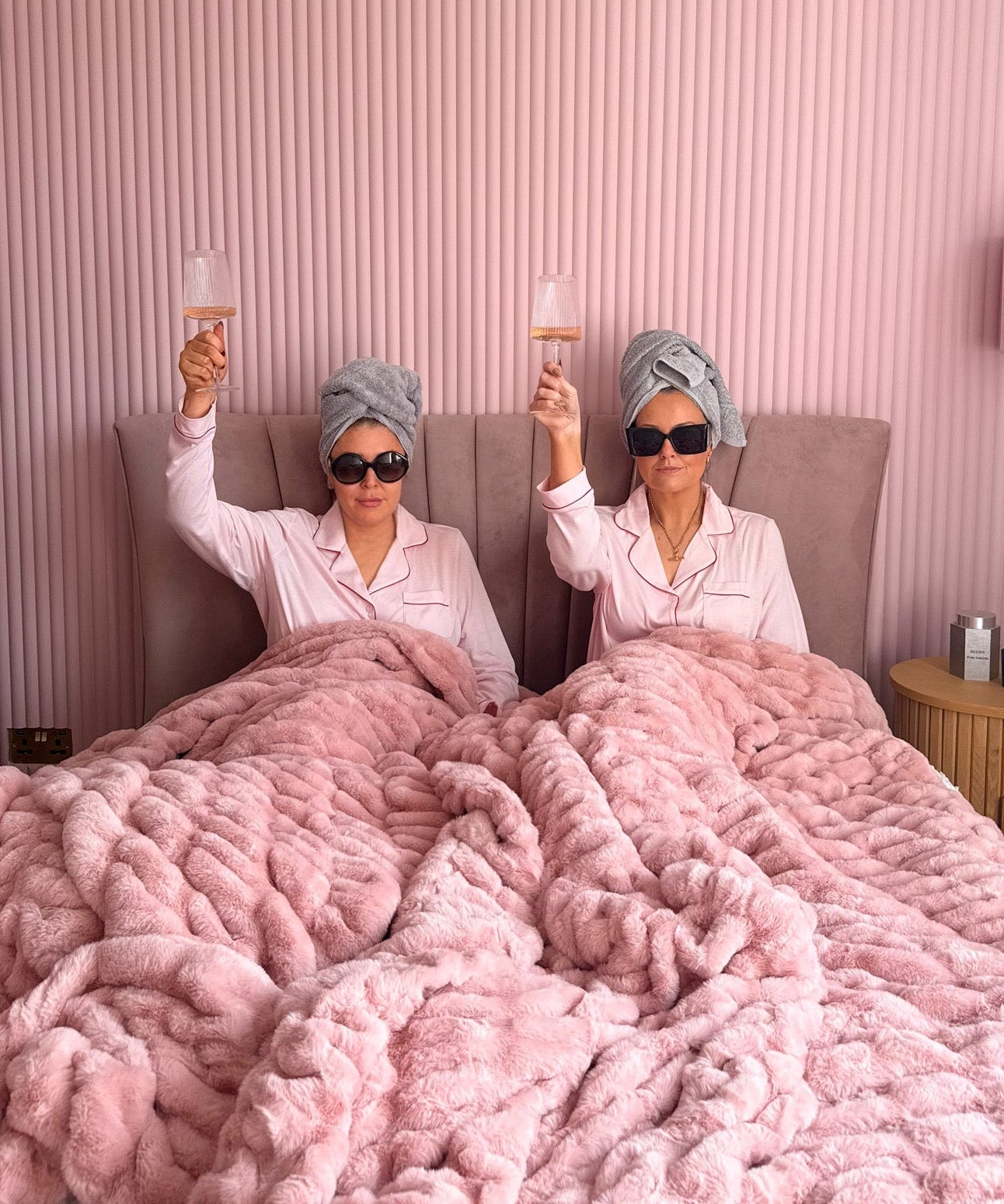 Two women in bed with pink blankets.