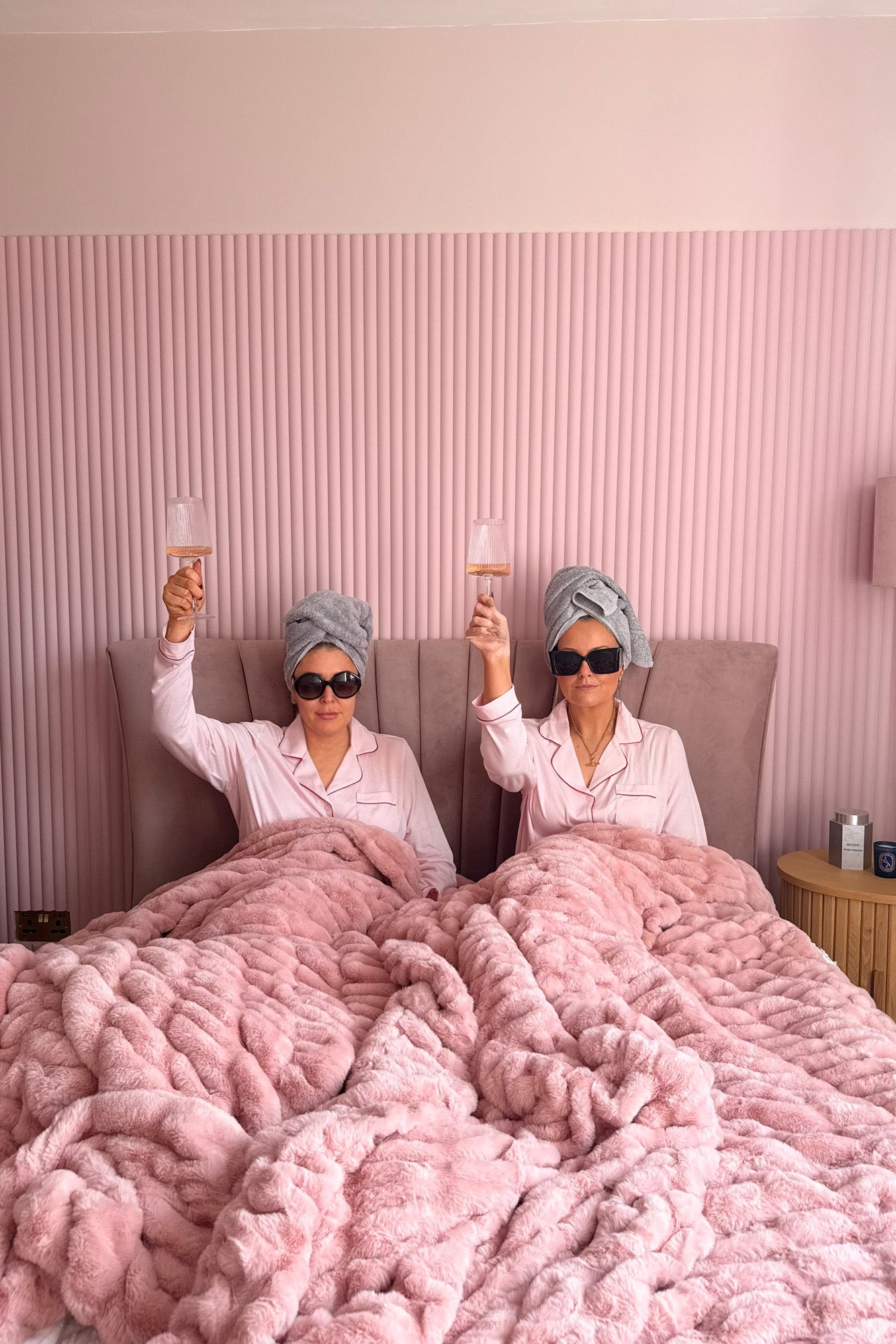 Two women in bed with pink blankets.