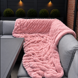 Pink fluffy faux fur blanket draped over a gray sofa on an outdoor patio.