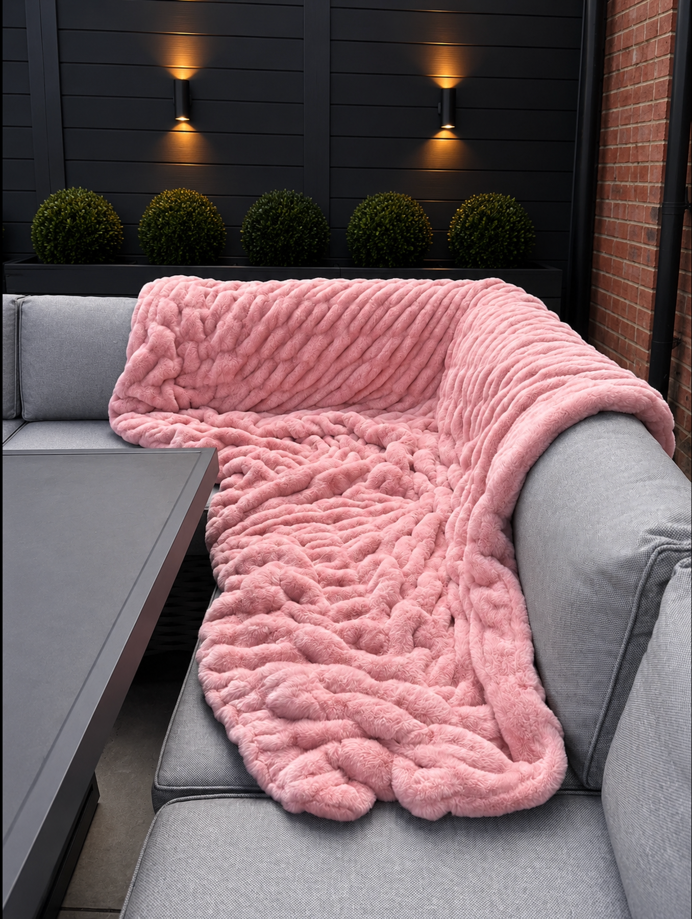 Pink fluffy faux fur blanket draped over a gray sofa on an outdoor patio.